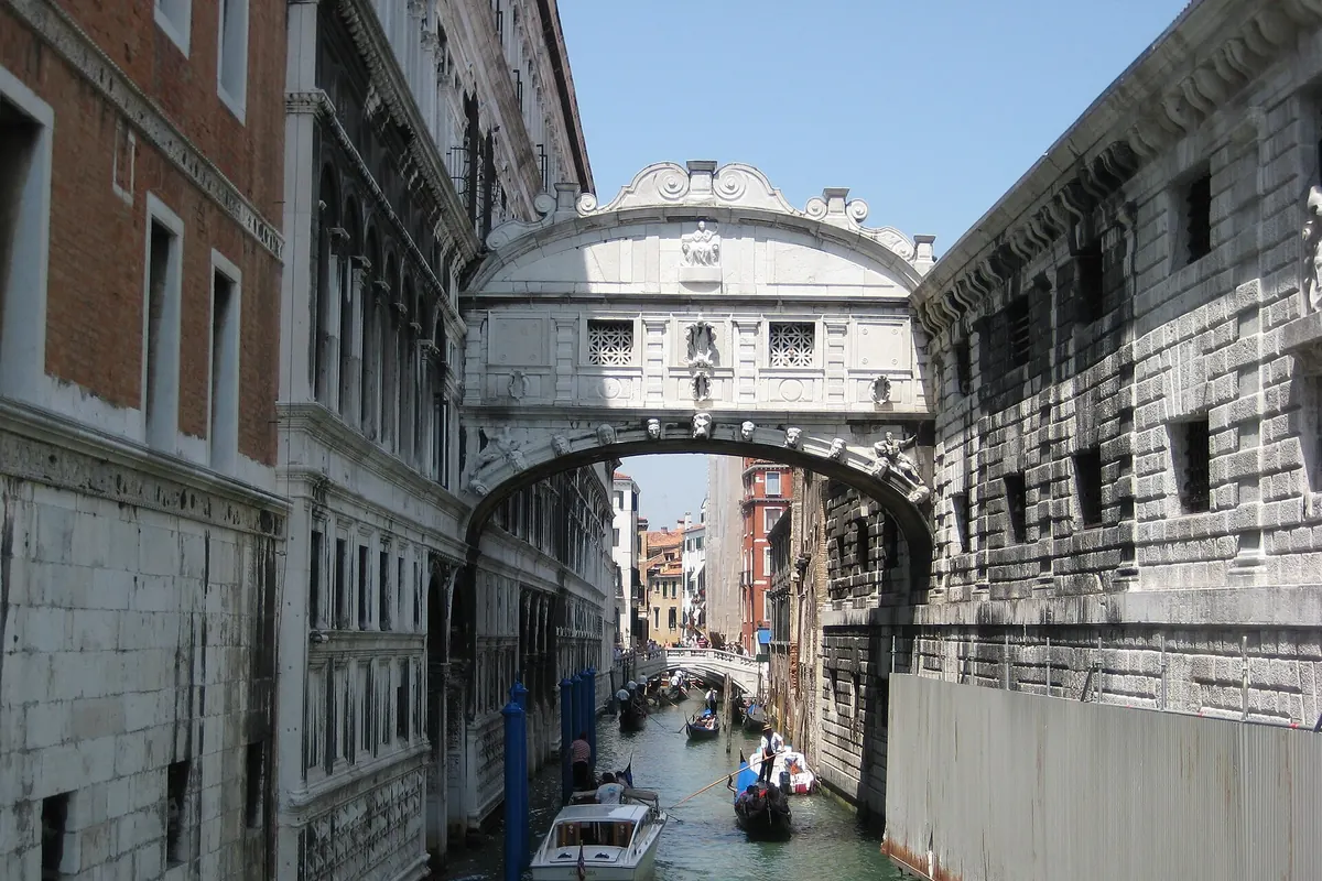 The Bridge of Sighs, an enclosed white stone bridge with two lattice windows, arching over a canal with gondolas below.