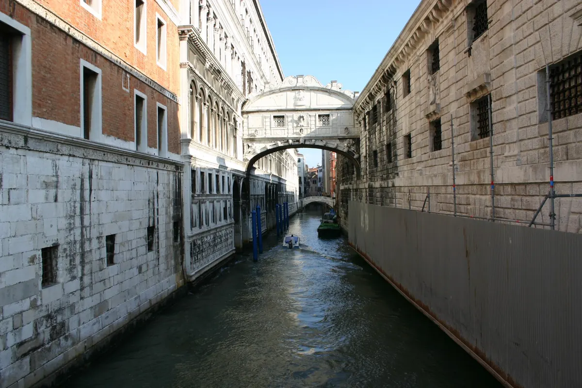 The Rio di Palazzo canal with the Bridge of Sighs in the distance, a stone wall with barred windows on the right and the Doge's Palace on the left.